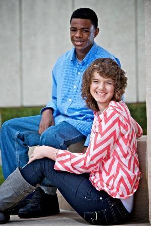 Two smiling teens sitting outside