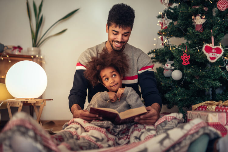 Dad readingeading a fairy tale to his son in front of the holiday tree